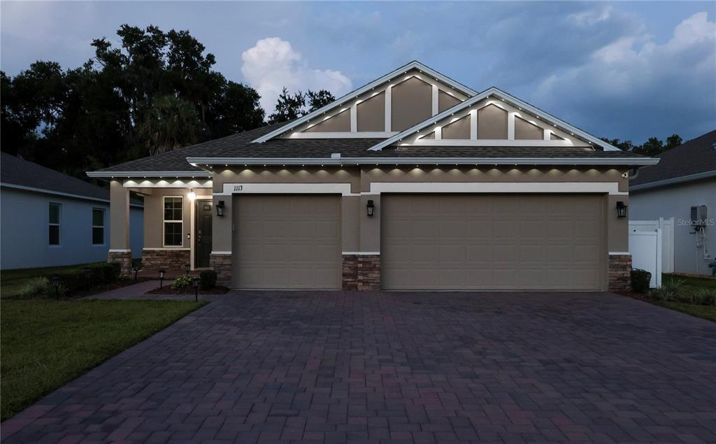 A single-story house with a paved driveway, two garage doors, and decorative exterior lighting — 1113 BRADFORD RIDGE DRIVE, LEESBURG, FL