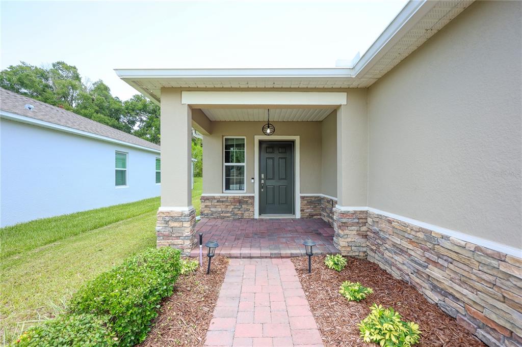 A front porch with a brick walkway, stone veneer accents, and a dark entry door — 1113 BRADFORD RIDGE DRIVE, LEESBURG, FL