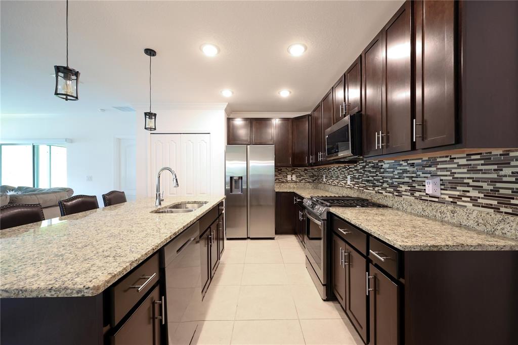 A kitchen features dark wood cabinets, granite countertops, stainless steel appliances, and a tiled backsplash — 1113 BRADFORD RIDGE DRIVE, LEESBURG, FL