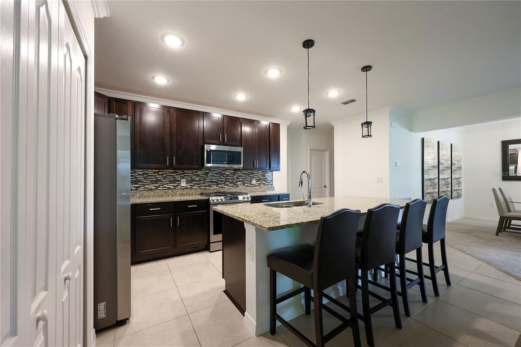 A kitchen with dark wood cabinets, granite countertops, a center island, and stainless steel appliances — 1113 BRADFORD RIDGE DRIVE, LEESBURG, FL
