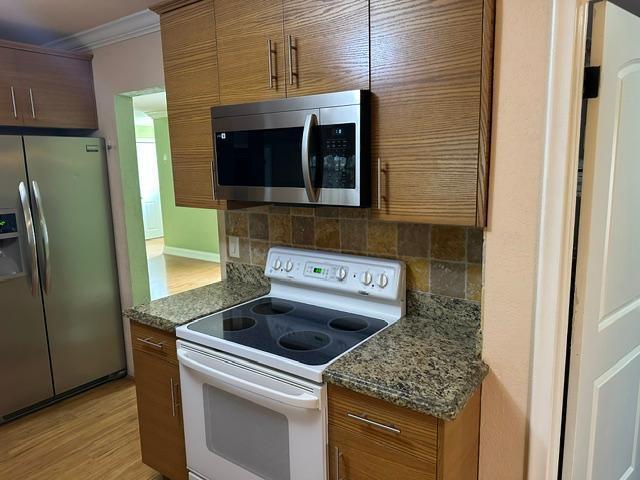 A kitchen features wood cabinets, stainless steel appliances, a white electric stove, and granite countertops — 732 SE 11th Avenue, Deerfield Beach FL 33441, DEERFIELD BEACH, FL