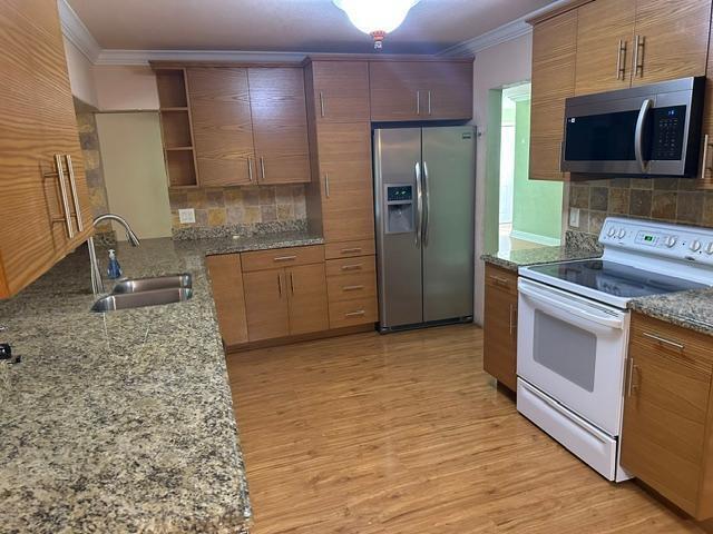 A kitchen features wood cabinets, granite countertops, stainless steel appliances, and light wood flooring — 732 SE 11th Avenue, Deerfield Beach FL 33441, DEERFIELD BEACH, FL