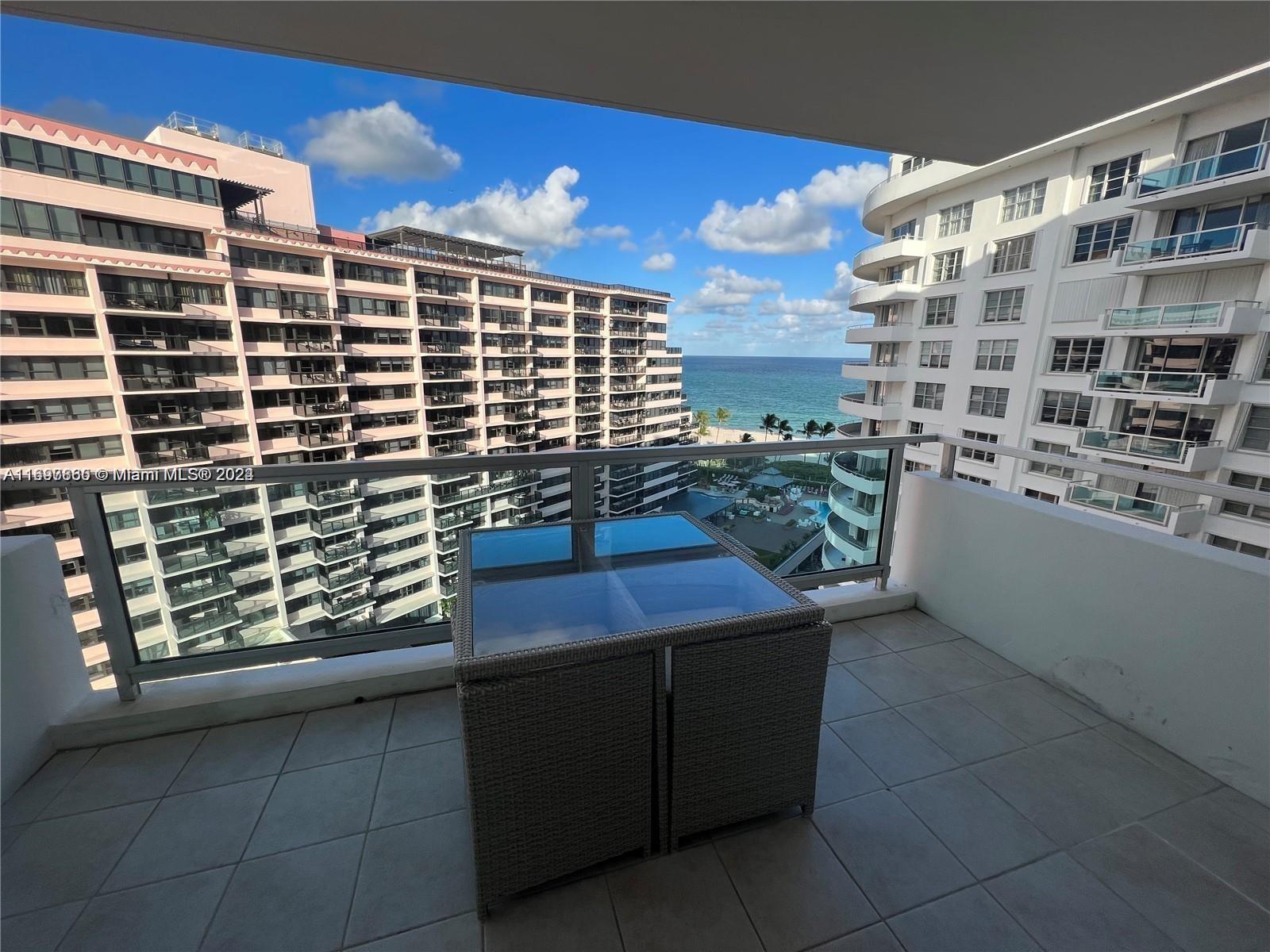 A balcony with a glass-topped table overlooks a beach between two large apartment buildings — 5161 COLLINS AVE # 1403, Miami Beach FL 33140, MIAMI BEACH, FL