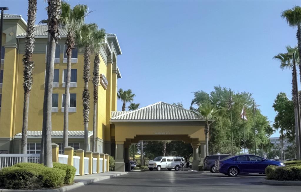 A yellow hotel building with a covered entrance and palm trees under a clear sky — 3000 MAINGATE LANE UNIT 530, KISSIMMEE, FL