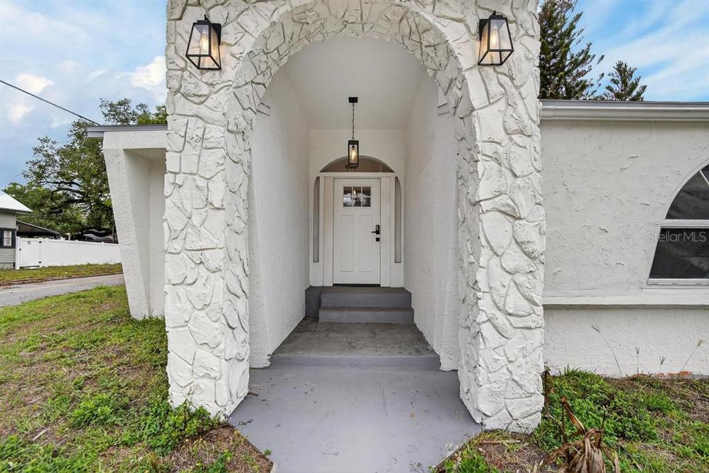 A white house exterior features a stone-faced arched entryway with a white front door — 800 N CHURCH AVENUE, MULBERRY, FL