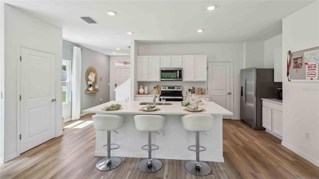 A modern kitchen features a large white island with bar stools and stainless steel appliances — 10549 TUCKER ROAD, WEEKI WACHEE, FL