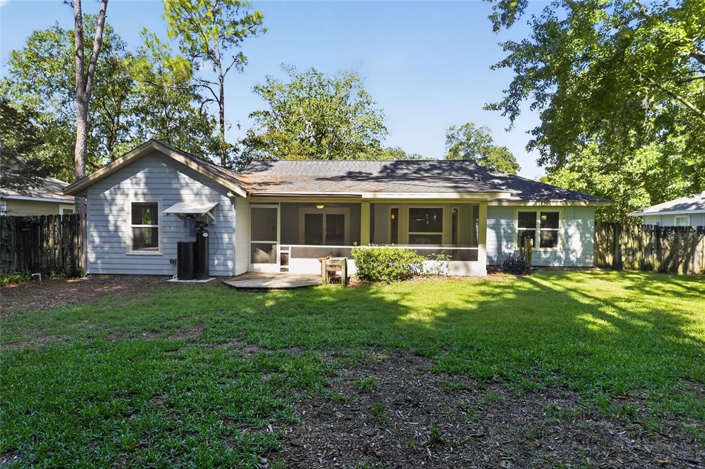 The backyard of a single-story house features a screened-in porch, wood siding, and mature trees — 6909 SW 80TH DRIVE, GAINESVILLE, FL