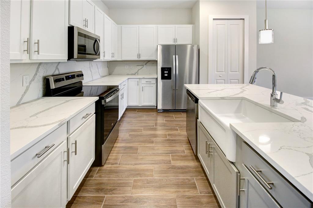 A modern kitchen features white cabinets, stainless steel appliances, and a farmhouse sink on an island — 1523 HERITAGE PLACE, OVIEDO, FL