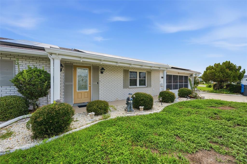 A single-story brick house with a yellow front door, white shutters, and a landscaped yard — 1811 MILFORD CIRCLE, SUN CITY CENTER, FL