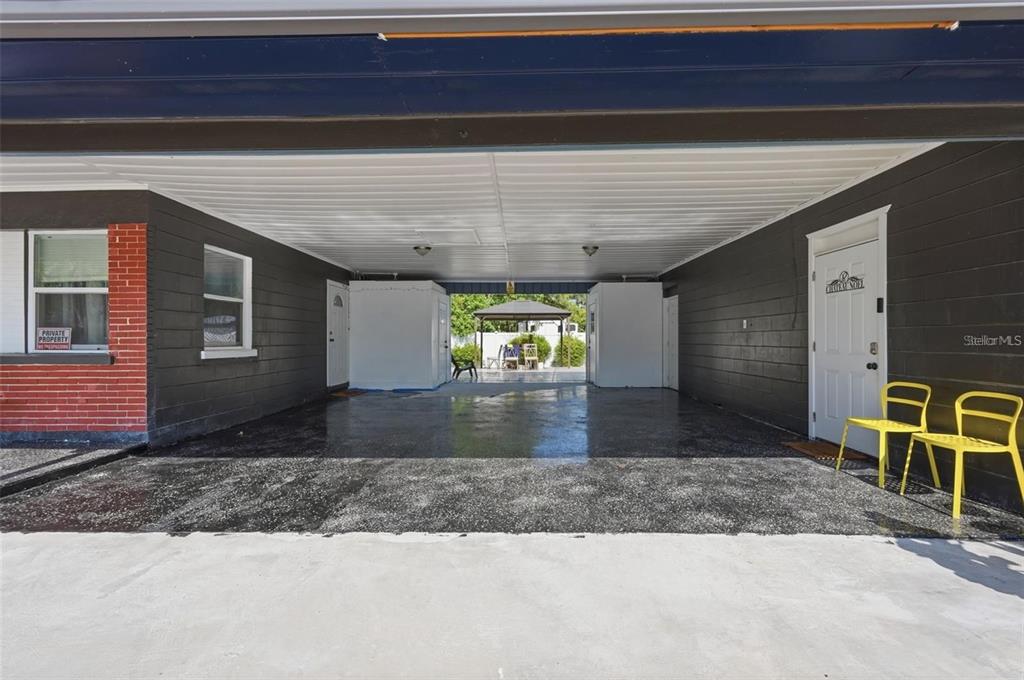A covered carport with a concrete floor, dark walls, and two yellow chairs — 10107 N ASTER AVENUE, TAMPA, FL