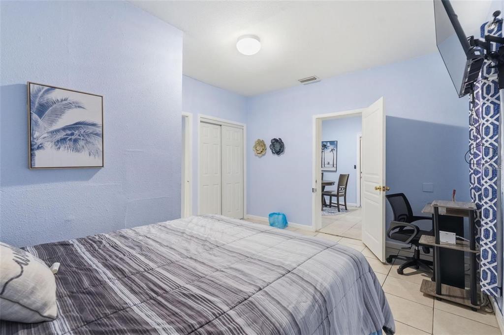 A bedroom with light blue walls, a striped bedspread, and a doorway leading to another room — 10107 N ASTER AVENUE, TAMPA, FL