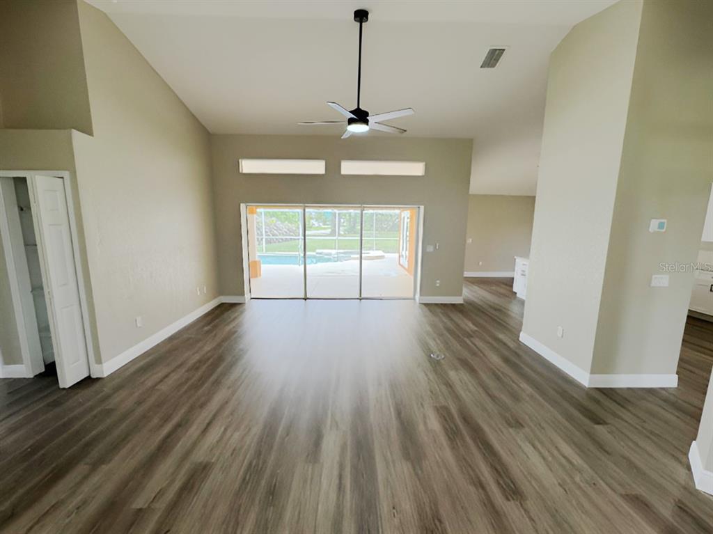 A living room with vaulted ceilings, wood-look flooring, a ceiling fan, and sliding glass doors — 13982 NAYLOR AVENUE, PORT CHARLOTTE, FL