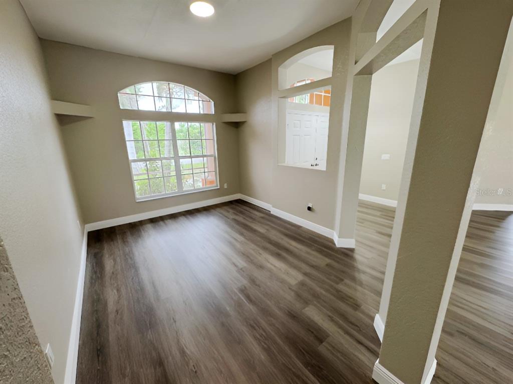 An empty room features wood-look flooring, beige walls, and a large arched window — 13982 NAYLOR AVENUE, PORT CHARLOTTE, FL