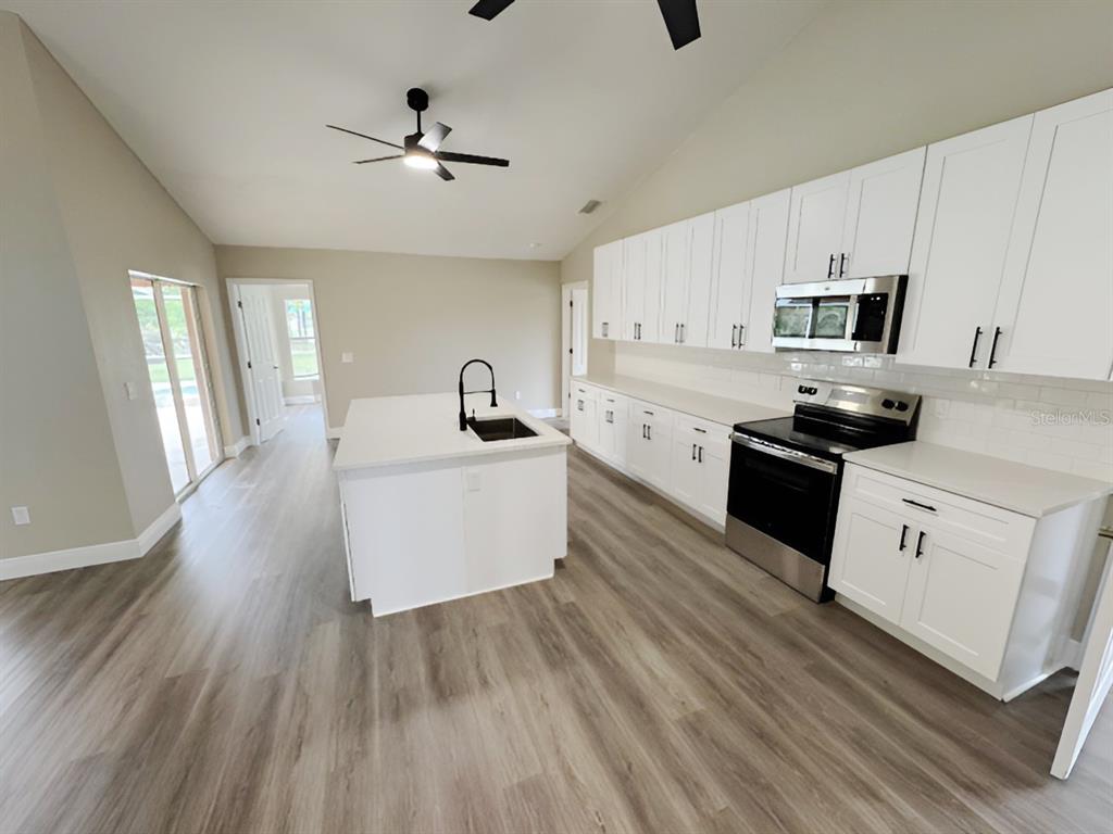A modern kitchen features white cabinets, stainless steel appliances, a center island, and wood-look flooring — 13982 NAYLOR AVENUE, PORT CHARLOTTE, FL