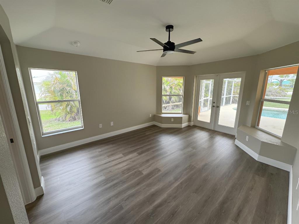 An empty room features wood-look flooring, a ceiling fan, large windows, and glass patio doors — 13982 NAYLOR AVENUE, PORT CHARLOTTE, FL