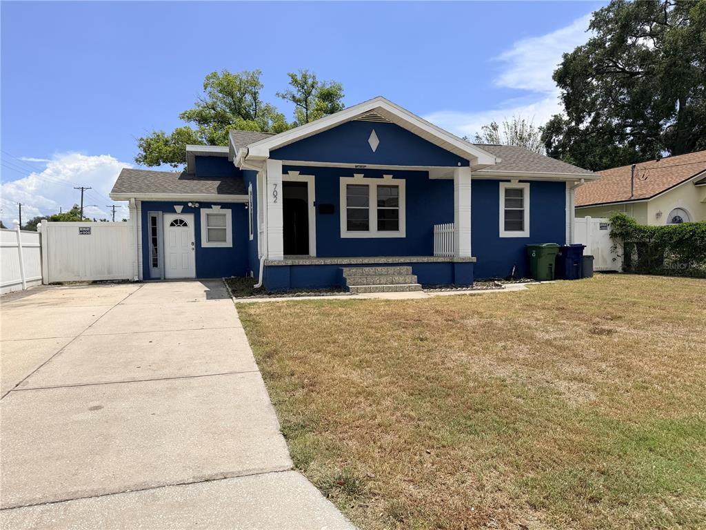 A blue single-story house with a concrete driveway, front porch, and a white fence — 702 W PENINSULAR STREET, TAMPA, FL