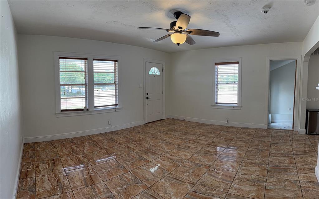 A living room features white walls, a ceiling fan, and brown marble-patterned tile flooring — 702 W PENINSULAR STREET, TAMPA, FL