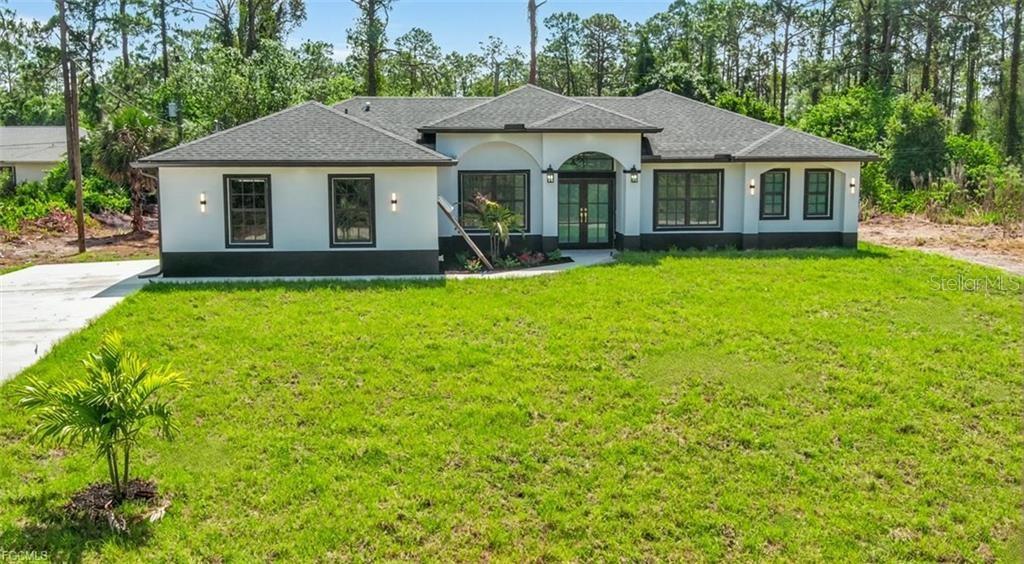 A single-story house with white stucco walls, dark trim, and a dark shingled roof — 1506 8TH AVENUE, LEHIGH ACRES, FL