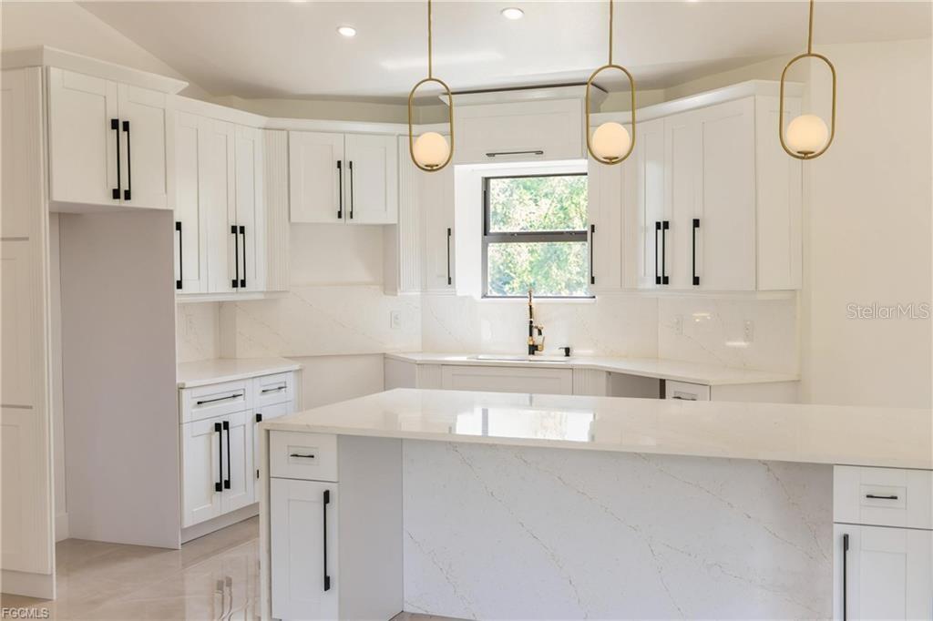 A modern kitchen features white shaker cabinets, quartz countertops, and three gold pendant lights — 1506 8TH AVENUE, LEHIGH ACRES, FL