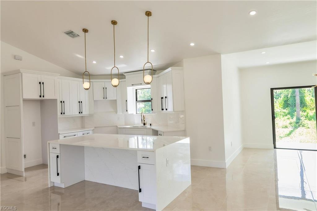 A modern kitchen features white cabinets, a large quartz island, and three pendant lights — 1506 8TH AVENUE, LEHIGH ACRES, FL