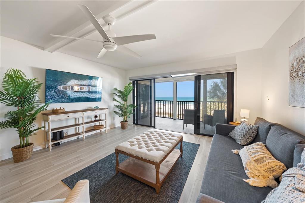 A living room features a grey sofa, tufted ottoman, and sliding doors opening to a balcony — 900 GULF BOULEVARD UNIT 204, INDIAN ROCKS BEACH, FL