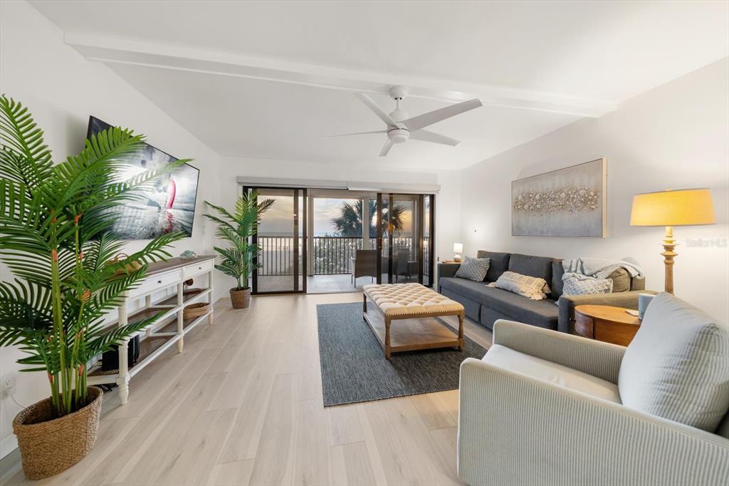 A living room features light wood floors, a gray sofa, and a balcony with ocean views — 900 GULF BOULEVARD UNIT 204, INDIAN ROCKS BEACH, FL