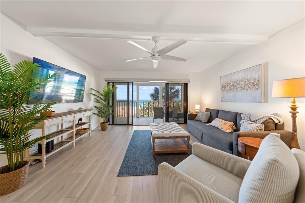 A living room with a gray sofa, white ottoman, and sliding doors leading to a balcony — 900 GULF BOULEVARD UNIT 204, INDIAN ROCKS BEACH, FL