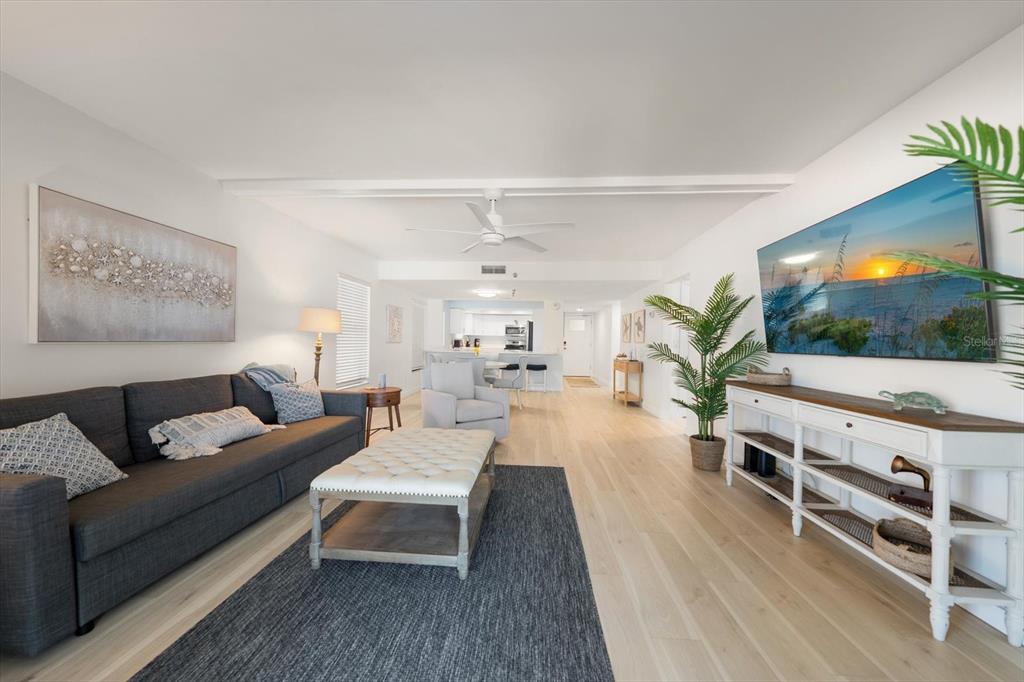 A living room features a gray sofa, white tufted ottoman, and a wall-mounted television — 900 GULF BOULEVARD UNIT 204, INDIAN ROCKS BEACH, FL