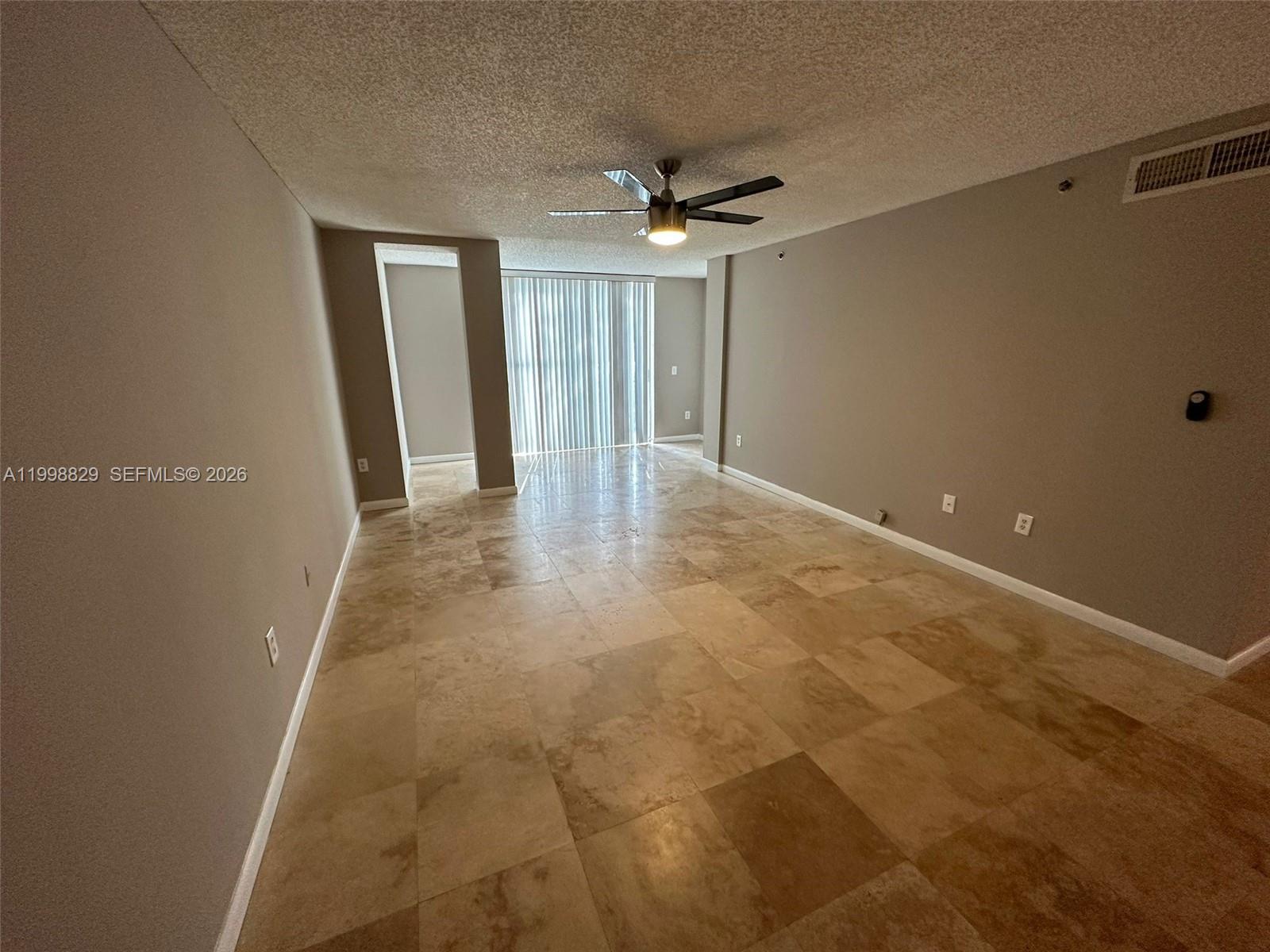 An empty room features beige tile flooring, a ceiling fan, and sliding glass balcony doors — 3113 Clint Moore Rd # 103, Boca Raton FL 33496, BOCA RATON, FL