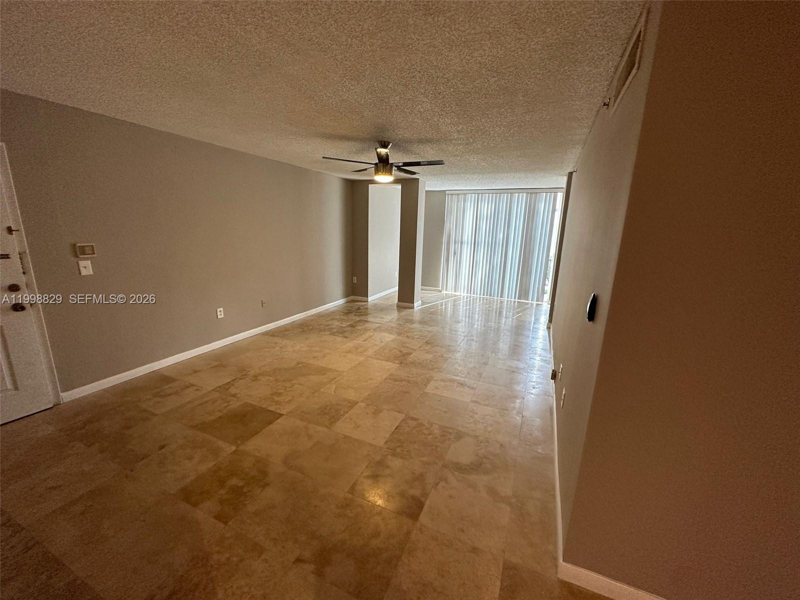 An empty living room features beige tile flooring, a ceiling fan, and vertical window blinds — 3113 Clint Moore Rd # 103, Boca Raton FL 33496, BOCA RATON, FL