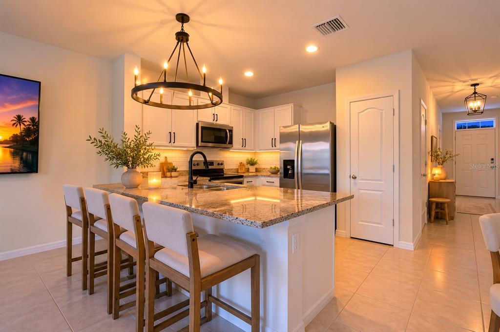 A kitchen features a granite-topped island with bar seating, white cabinetry, and a chandelier — 1767 WOODEN STREET, DAVENPORT, FL