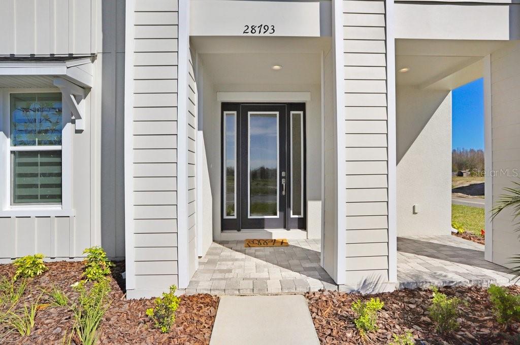 The exterior view shows a front entrance with a dark door and a paved porch — 28793 SWEET PERSIMMON DRIVE, WESLEY CHAPEL, FL
