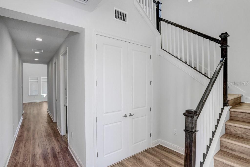 A bright entryway features wood-look flooring, white walls, a double-door closet, and a wooden staircase — 28793 SWEET PERSIMMON DRIVE, WESLEY CHAPEL, FL