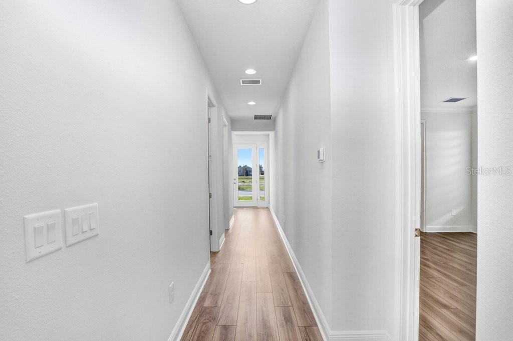 A bright hallway with light wood-look flooring leads to a glass-paneled exterior door — 28793 SWEET PERSIMMON DRIVE, WESLEY CHAPEL, FL