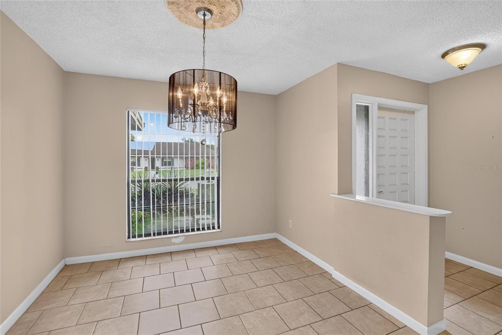 A dining area with beige walls, tile flooring, a crystal chandelier, and a large window — 1201 SANDALWOOD DRIVE, PLANT CITY, FL