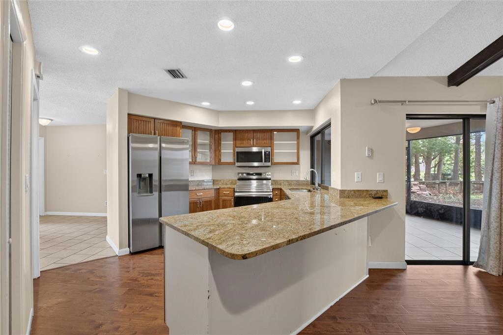 A kitchen with wood cabinets, granite countertops, stainless steel appliances, and a sliding glass door — 1201 SANDALWOOD DRIVE, PLANT CITY, FL