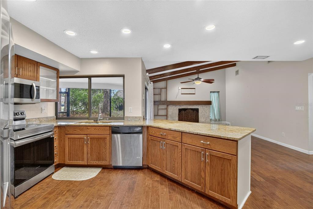 A kitchen with wood cabinets, granite countertops, and stainless steel appliances opens to a living area — 1201 SANDALWOOD DRIVE, PLANT CITY, FL