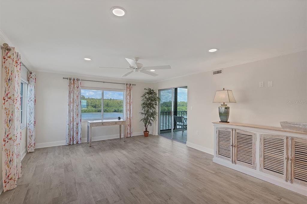 A bright living room features light wood-look flooring, a ceiling fan, and a waterfront balcony — 9397 MIDNIGHT PASS ROAD UNIT 501, SARASOTA, FL