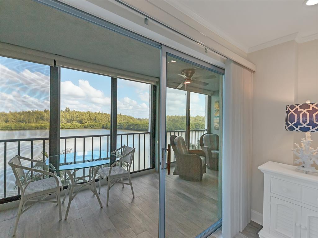 A glass-enclosed balcony with a dining set overlooks a body of water and trees — 9397 MIDNIGHT PASS ROAD UNIT 501, SARASOTA, FL