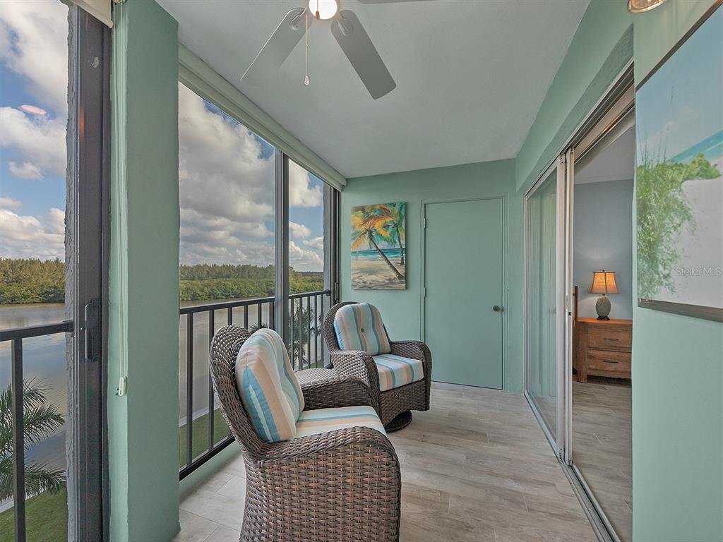 A screened-in balcony features two wicker chairs, light tile flooring, and a view of water — 9397 MIDNIGHT PASS ROAD UNIT 501, SARASOTA, FL