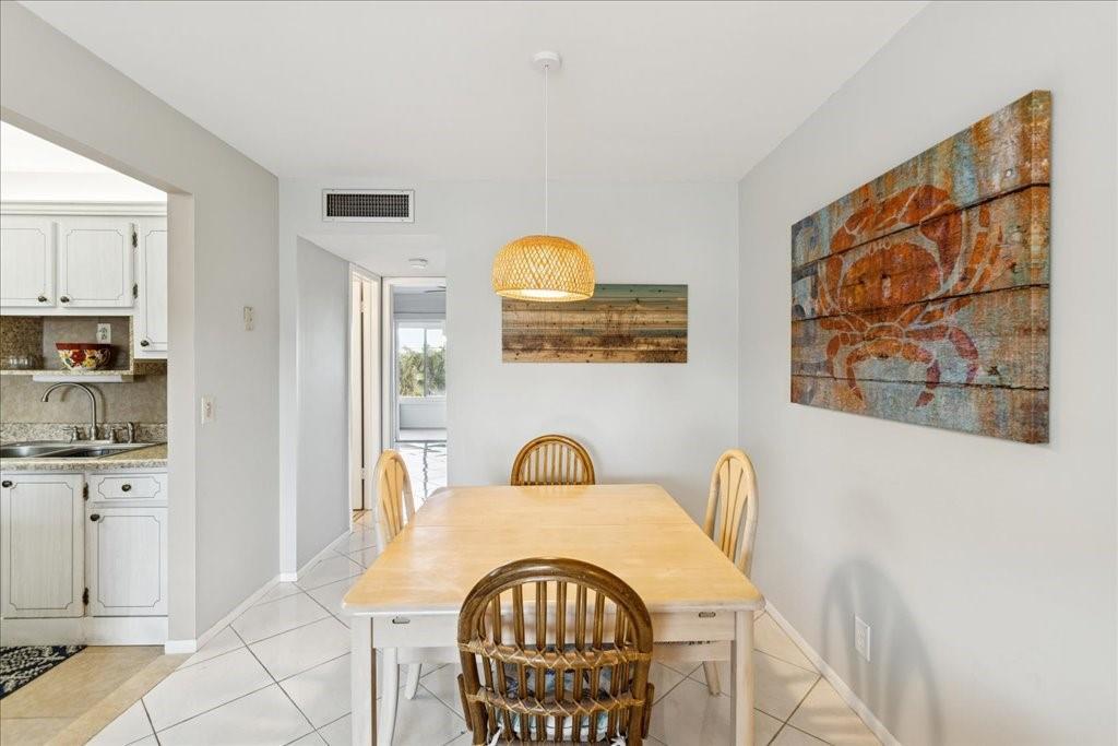 A dining area features a wooden table, wicker chairs, a pendant light, and coastal wall art — 95 North Boulevard # 2b, Boynton Beach FL 33435, BOYNTON BEACH, FL