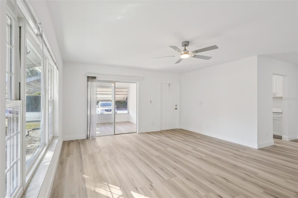 A bright living room features light wood-look flooring, white walls, a ceiling fan, and sliding doors — 11147 ACME DRIVE UNIT D, ORLANDO, FL