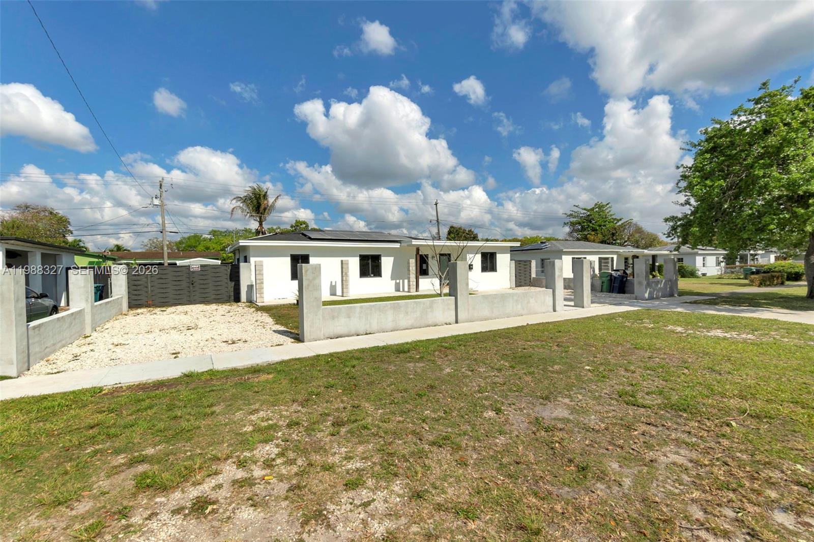 A white single-story house features a concrete perimeter wall and a gravel driveway — 14520 Carver Drive, Miami FL 33176, MIAMI, FL