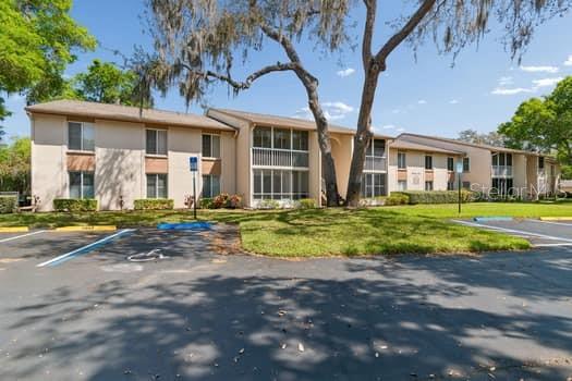 A two-story apartment building with beige siding and screened-in balconies sits behind a parking lot — 13103 CYPRESS HILL DRIVE UNIT B2, HUDSON, FL