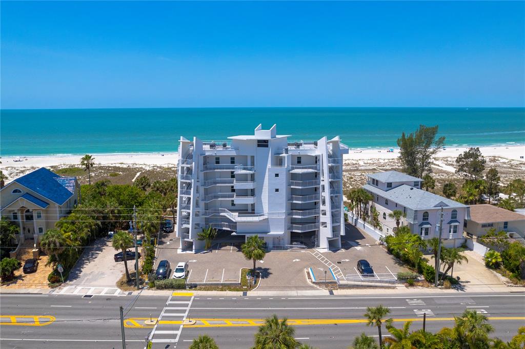 An aerial view of a white multi-story beachfront condominium building located across from a road — 10116 GULF BOULEVARD UNIT 403W, TREASURE ISLAND, FL