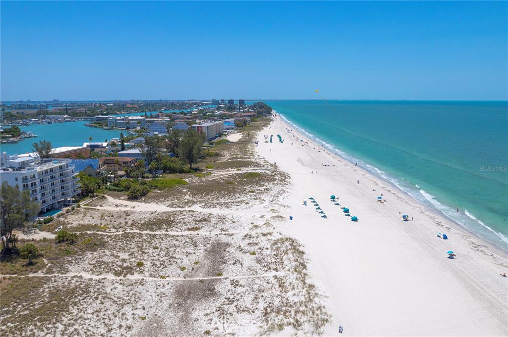 An aerial view shows a white sand beach, turquoise water, and nearby coastal buildings — 10116 GULF BOULEVARD UNIT 403W, TREASURE ISLAND, FL