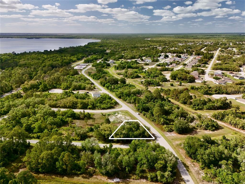 An aerial view shows a vacant, wooded lot outlined in white along a paved road — 634 MEDITERRANEAN COURT, KISSIMMEE, FL