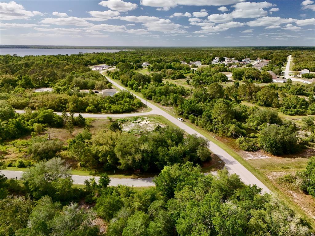 An aerial view shows a vacant, tree-covered lot situated at a road intersection near a lake — 634 MEDITERRANEAN COURT, KISSIMMEE, FL