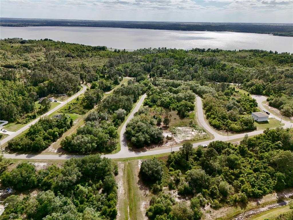 An aerial view shows a residential neighborhood with paved roads, wooded lots, and a lake — 634 MEDITERRANEAN COURT, KISSIMMEE, FL