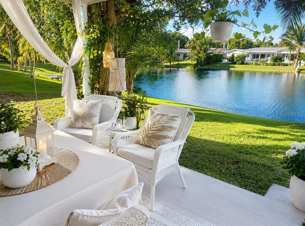A patio with white wicker chairs overlooks a grassy lawn and a calm lake — 7551 SW 42ND PLACE, DAVIE, FL
